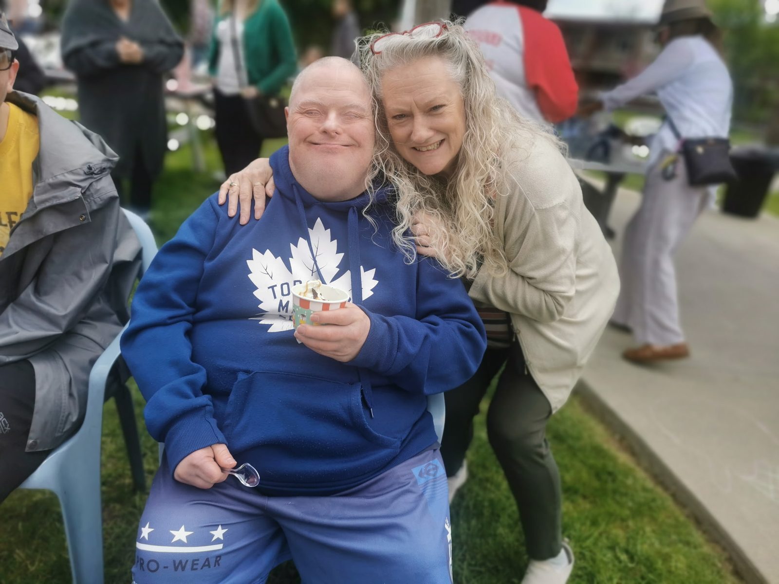 A man enjoying an ice cream beside a staff member at an outdoor community gathering