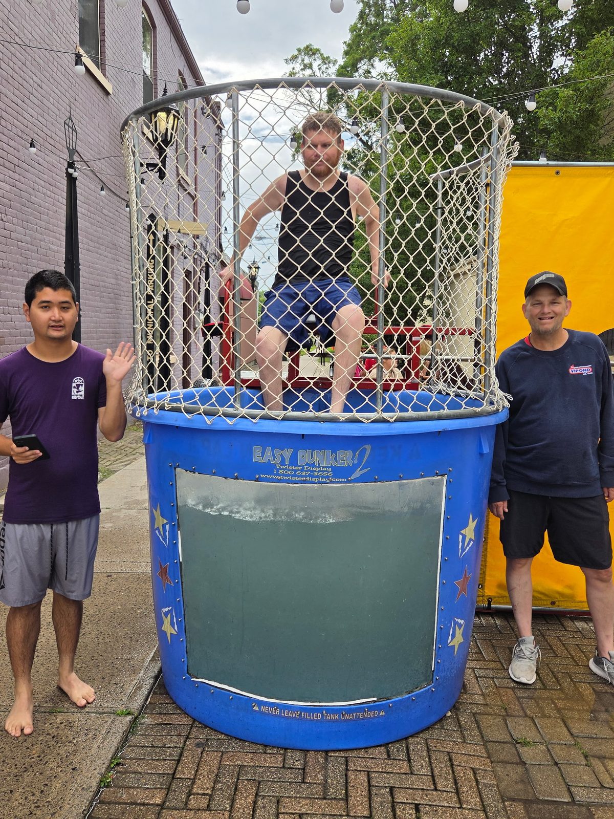Three people taking part in a dunk tank fundraiser at an outdoor community street event